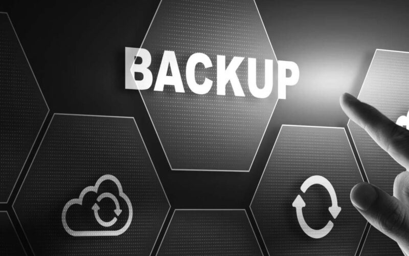 A hand points toward a glowing hexagon labeled BACKUP on a digital interface, surrounded by icons representing cloud storage, data synchronization, and files—perfect for illustrating a reliable backup or data recovery guide.