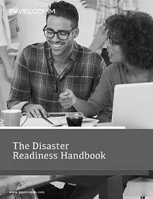 Two people sit at a table, smiling and talking while looking at documents about Disaster Recovery. A coffee mug and laptop are in front of them. The cover text reads “The Disaster Readiness Handbook.”.