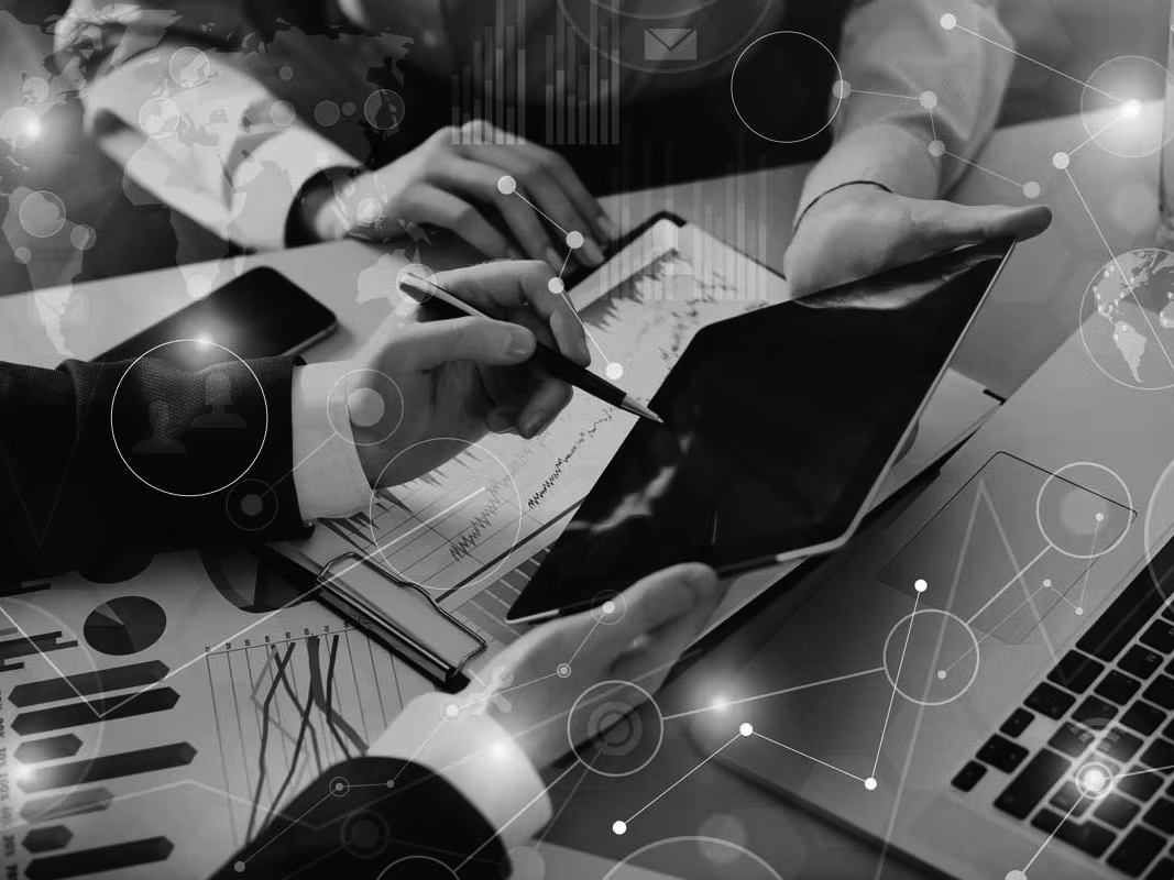 Three people collaborate at a desk with charts, a laptop, and a tablet, discussing data and analytics. Digital graphics highlight cloud computing and network connections, emphasizing teamwork and the advantages of technology in business analysis.