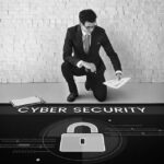 A man in a suit kneels on one knee, holding papers next to a clipboard. He faces a floor graphic with CYBER SECURITY and a padlock icon, highlighting IT security awareness for Portland businesses.