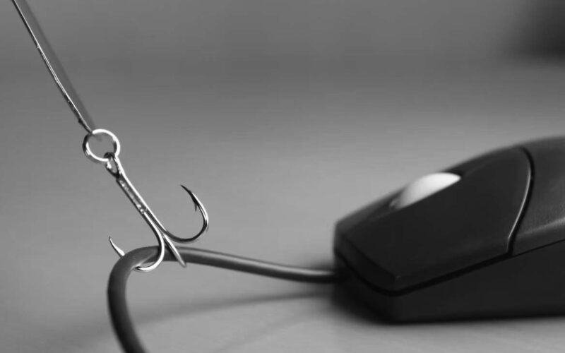 A fishing hook is caught on the cord of a computer mouse, symbolizing phishing or internet scams, with a focus on Phishing Prevention against a blurred background.