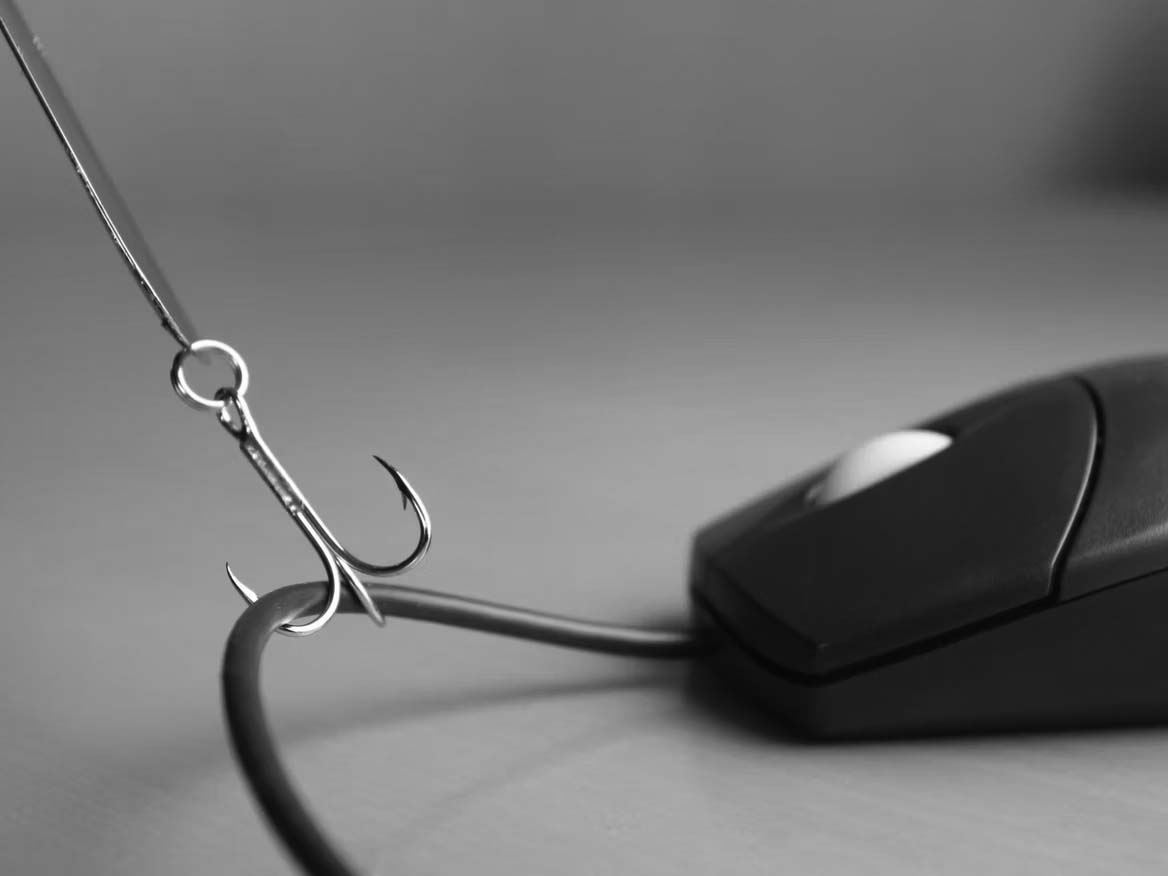 A fishing hook is caught on the cord of a computer mouse, symbolizing phishing or internet scams, with a focus on Phishing Prevention against a blurred background.
