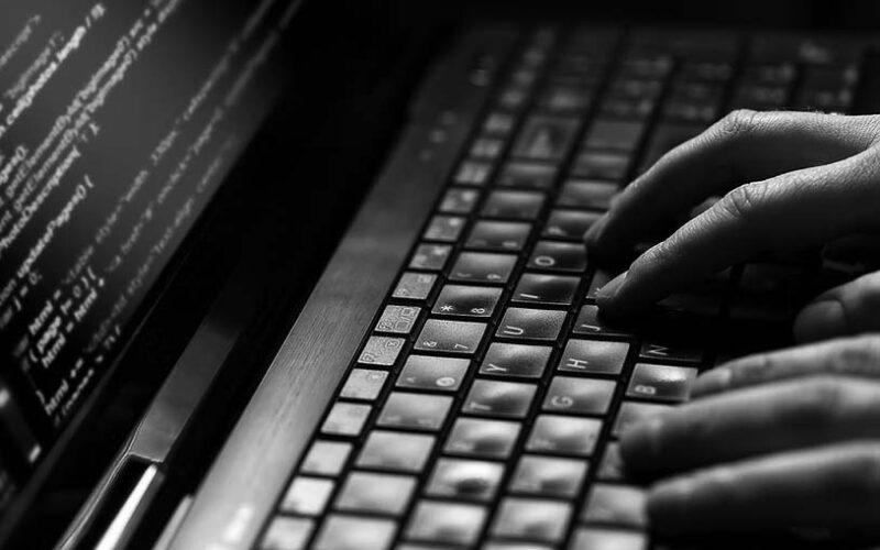 Close-up of hands typing on a laptop keyboard with lines of code visible on the screen, highlighting efforts to safeguard against ransomware and protect business security through coding activity.