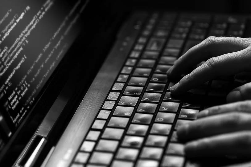 Close-up of hands typing on a laptop keyboard with lines of code visible on the screen, highlighting efforts to safeguard against ransomware and protect business security through coding activity.