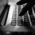 Close-up of a remote worker’s fingers typing on a glowing laptop keyboard with pink and blue lighting, creating a futuristic and tech-focused atmosphere.
