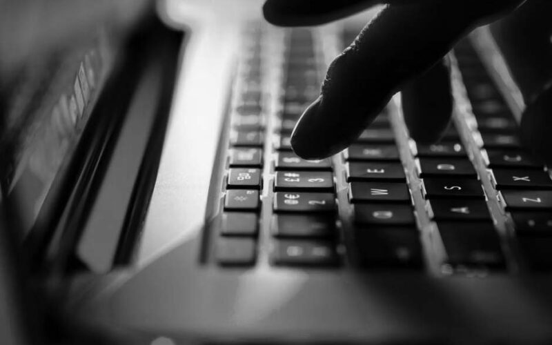 Close-up of a remote worker’s fingers typing on a glowing laptop keyboard with pink and blue lighting, creating a futuristic and tech-focused atmosphere.