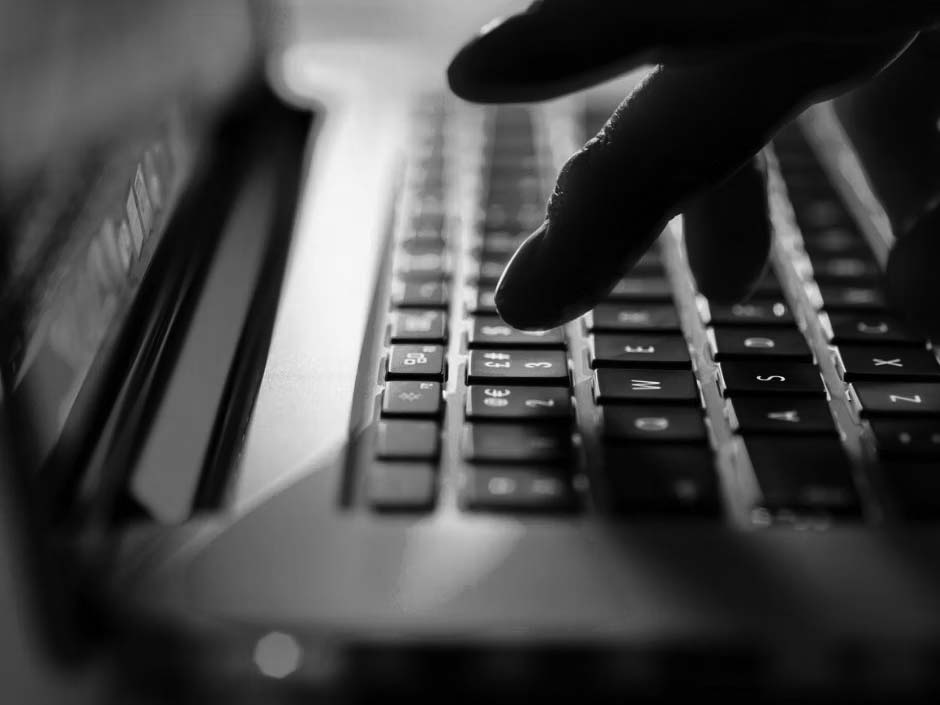 Close-up of a remote worker’s fingers typing on a glowing laptop keyboard with pink and blue lighting, creating a futuristic and tech-focused atmosphere.