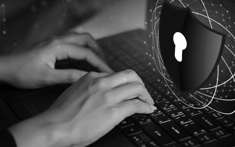Hands typing on a laptop keyboard with a digital graphic of a shield and padlock symbol, representing cybersecurity, data protection, and overcoming compliance obstacles.