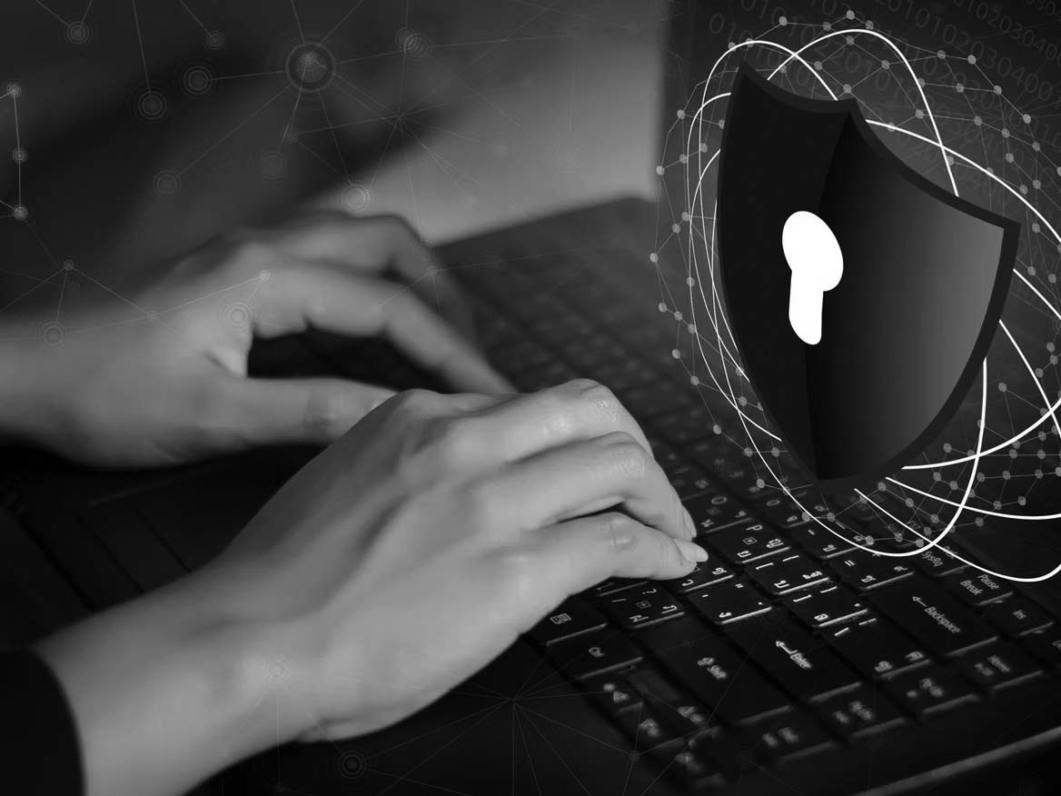 Hands typing on a laptop keyboard with a digital graphic of a shield and padlock symbol, representing cybersecurity, data protection, and overcoming compliance obstacles.