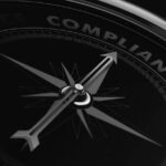 A close-up of a black compass with the needle pointing to the word COMPLIANCE—highlighted in blue and red accents—symbolizes regulatory compliance and professional compliance solutions.