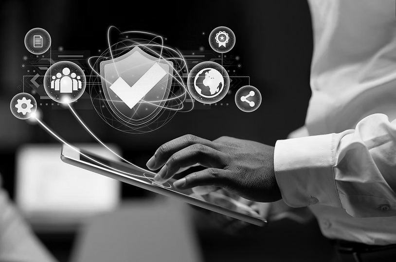 A person uses a tablet with a digital overlay of a shield checkmark icon and various technology and security symbols, illustrating IT security and measures to secure your IT against threats like ransomware.