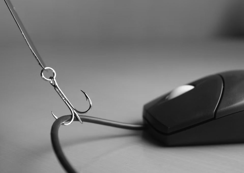 mouse-hook A fishing hook is attached to the cable of a computer mouse, symbolizing the concept of online phishing or internet scams. The image conveys the importance of anti-phishing measures. The background is out of focus.