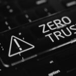 A glowing key with an exclamation mark warning symbol and the words ZERO TRUST sits on a dark computer keyboard, representing network security and the importance of zero trust network security in today’s evolving threat landscape.
