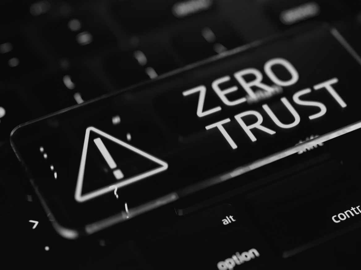 A glowing key with an exclamation mark warning symbol and the words ZERO TRUST sits on a dark computer keyboard, representing network security and the importance of zero trust network security in today’s evolving threat landscape.