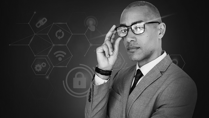 A man in a gray suit and glasses stands confidently, touching his glasses, with digital security icons and hexagonal patterns in the background, representing cybersecurity, technology, and Pavelcomm’s expertise in Strategic IT Planning.