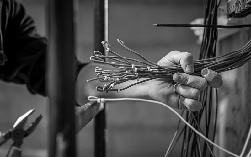 A person holds a bundle of Structured Cabling with yellow connectors, preparing for installation—a step toward future-proofing and enhancing a business network. Other wires and electrical tools are visible in the background.