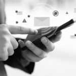A person uses a smartphone, with illustrated email icons, warning signs, and virus symbols appearing above the device, highlighting the need for phishing training to improve email security and enhance phishing prevention.